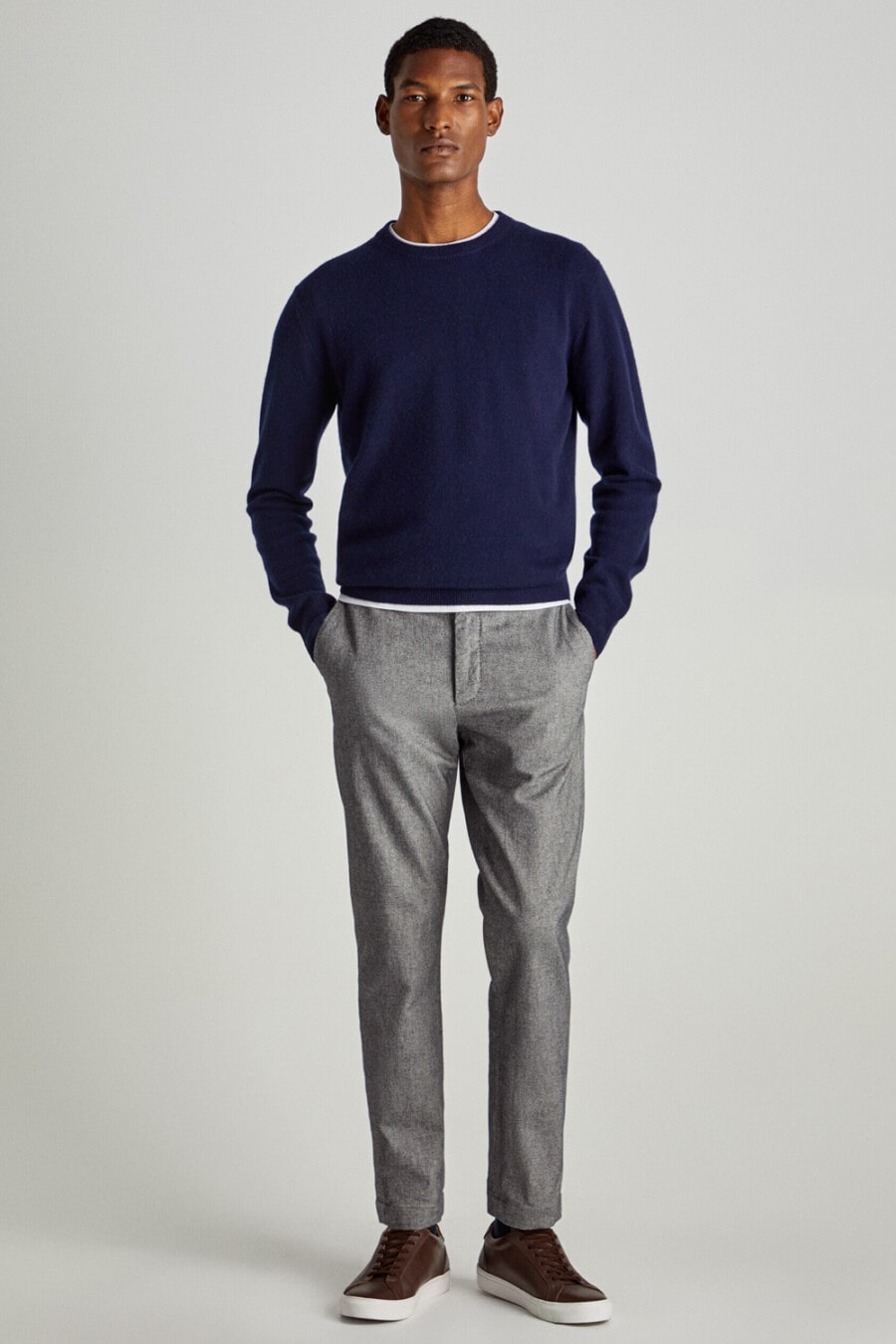 Men's grey textured pants, white T-shirt, navy crew-neck sweater and brown leather sneakers outfit