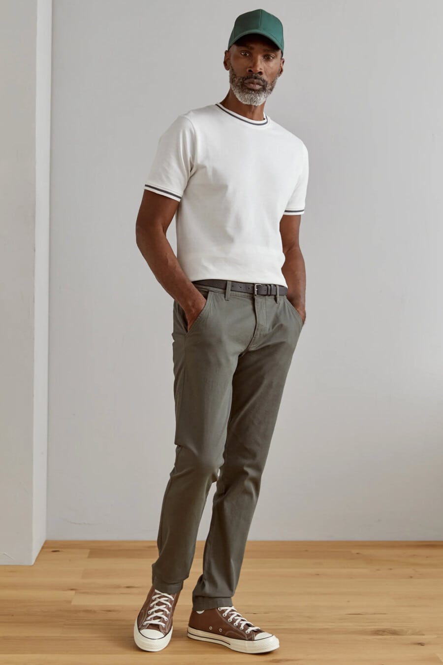 Men's mid-grey pants, white knitted T-shirt, green baseball cap and brown canvas high-top sneakers outfit