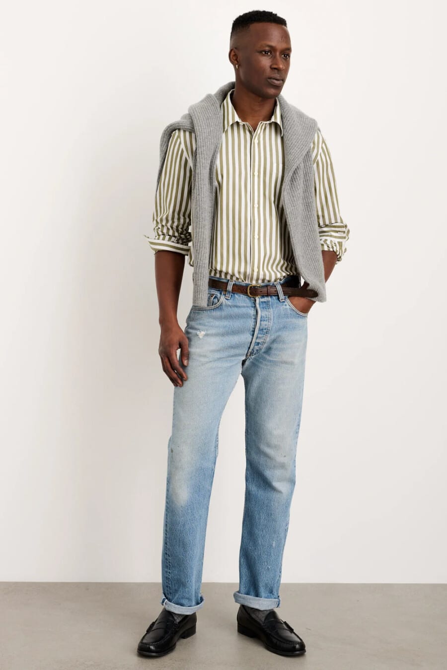 Men's light wash jeans, green/white stripe shirt, black leather penny loafers and grey ribbed sweater outfit