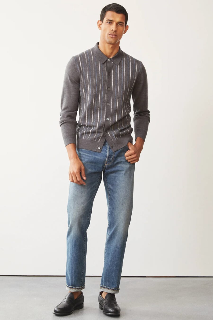 Men's mid-wash jeans, grey long-sleeve button-up polo shirt and black leather penny loafers worn sockless outfit