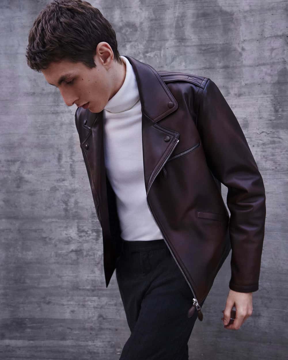Man wearing brown leather burnished Berluti biker jacket with a white turtleneck and black pants