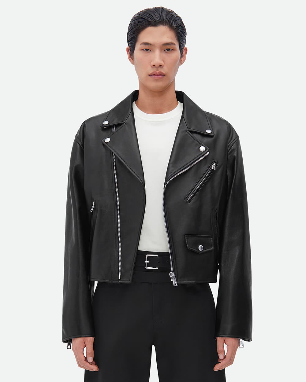 Asian man wearing black leather biker jacket by Bottega Veneta with a white T-shirt and black belted pants