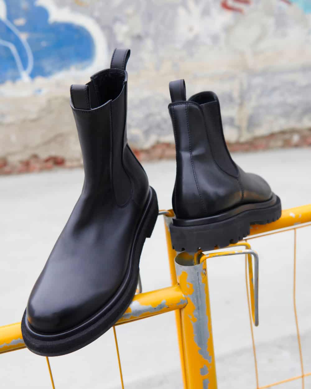 A pair of black leather Officine Creative Chelsea boots with chunky lug sole on top of a fence