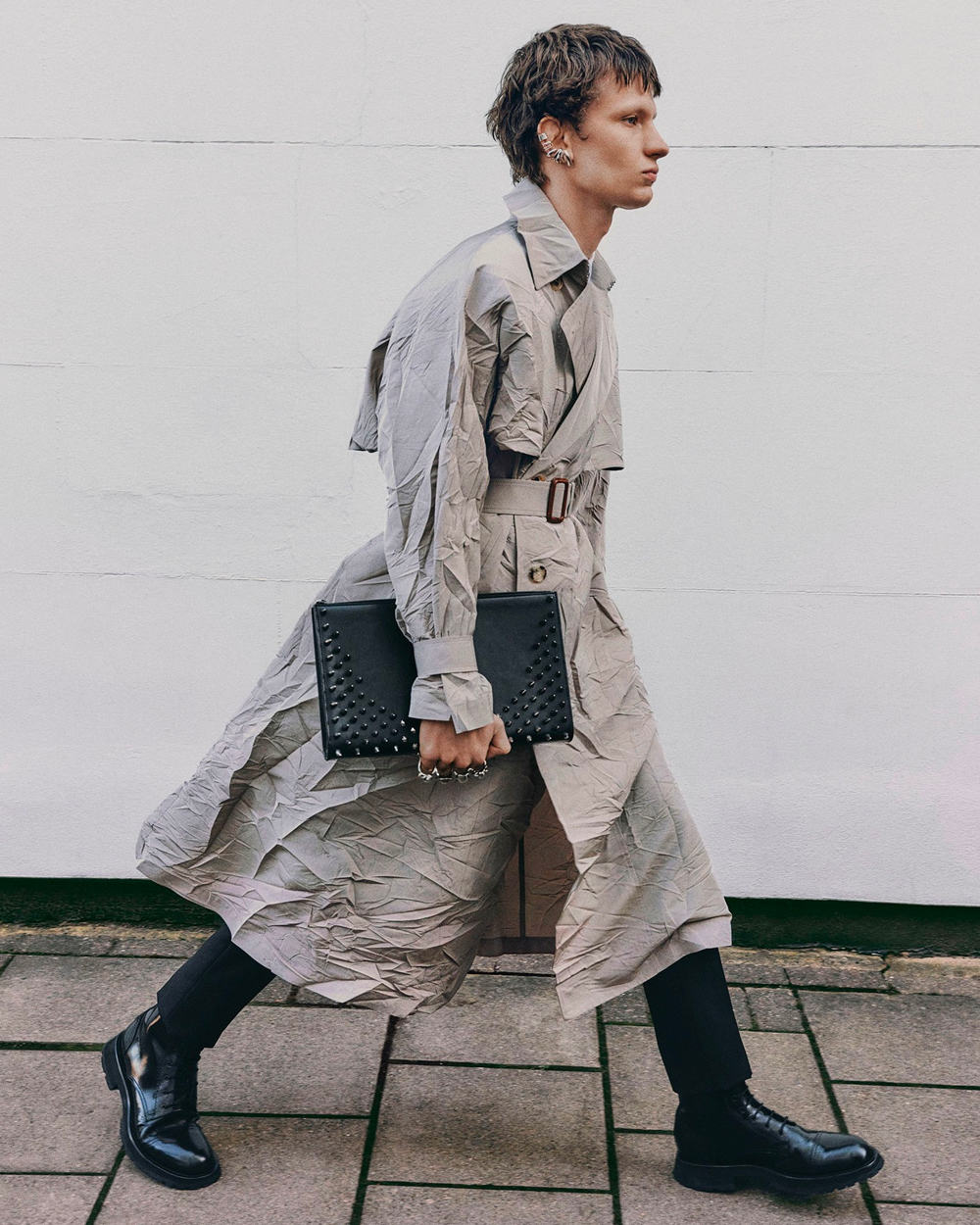 Man wearing Alexander McQueen long grey trench coat, black pants and black leather boots