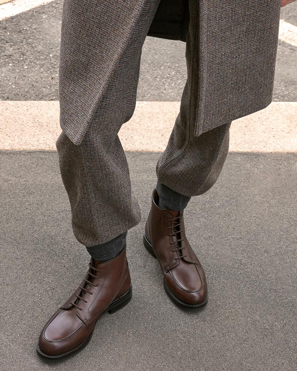A pair of men's Church's brown leather Derby boots worn on feet with charcoal socks and brown tweed pants