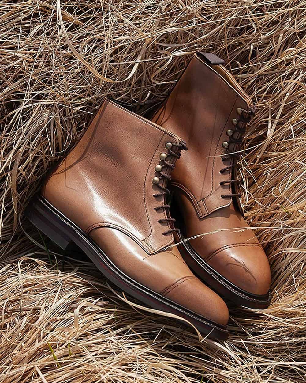 A pair of Crockett & Jones light brown leather men's military boots on a hay bale
