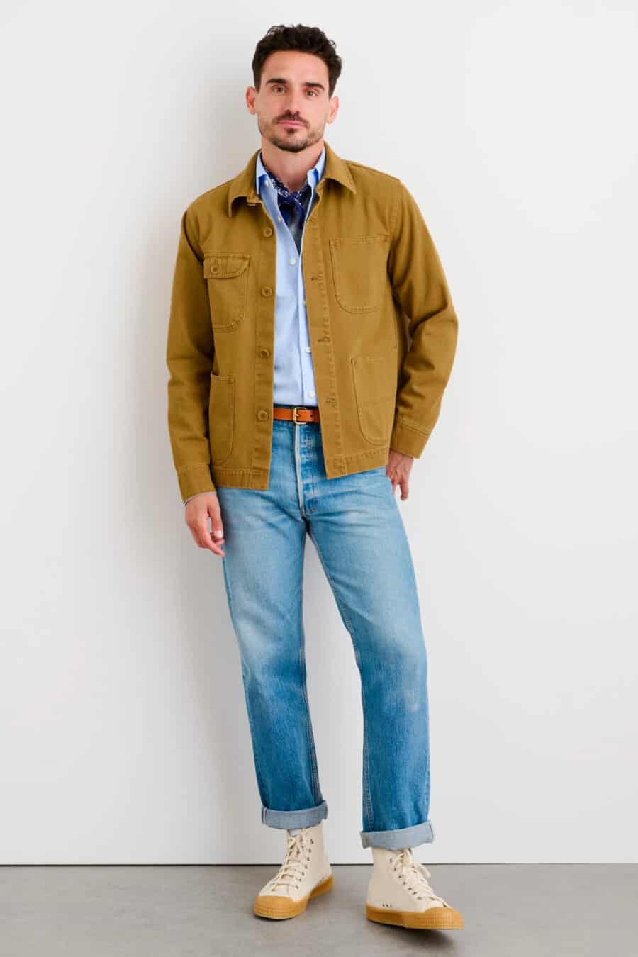 Men's light wash jeans, tucked in light blue shirt, tan cotton shacket and beige gumsole canvas high-top sneakers outfit