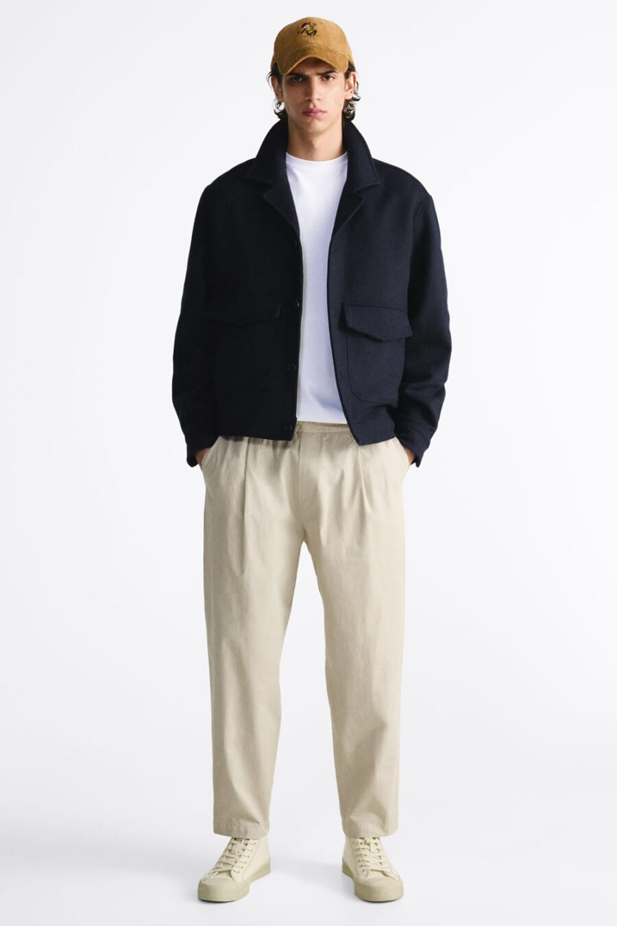 Men's wide-leg beige pleated pants, white T-shirt, navy wool blouson jacket, ta baseball cap and beige canvas high-top sneakers outfit