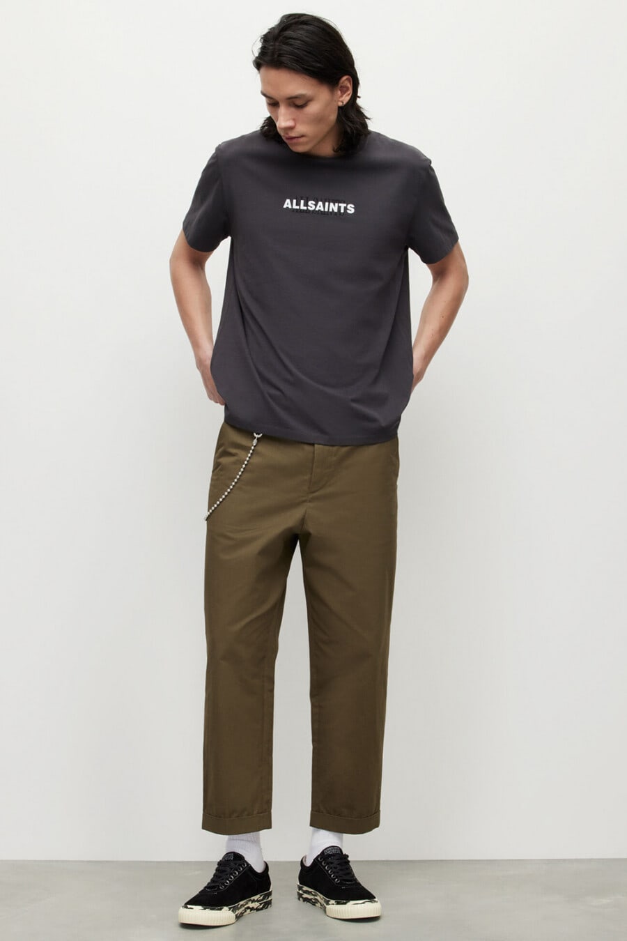 Men's khaki green cropped wide-leg chinos, black logo T-shirt, white socks, black canvas sneakers and wallet chain outfit 