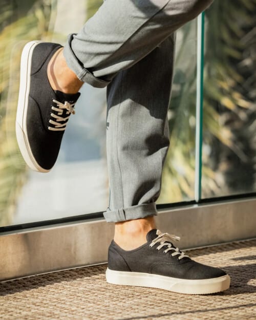 CLAE August canvas sneaker in black hemp worn sockless on feet with grey jeans