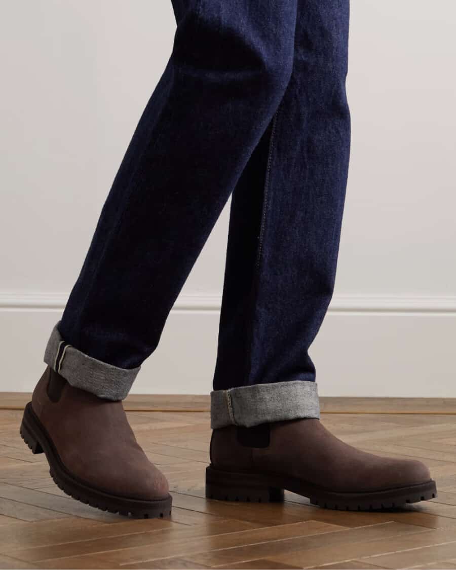 Pair of brown Common Projects Chelsea boots worn on feet with dark raw selvedge denim jeans
