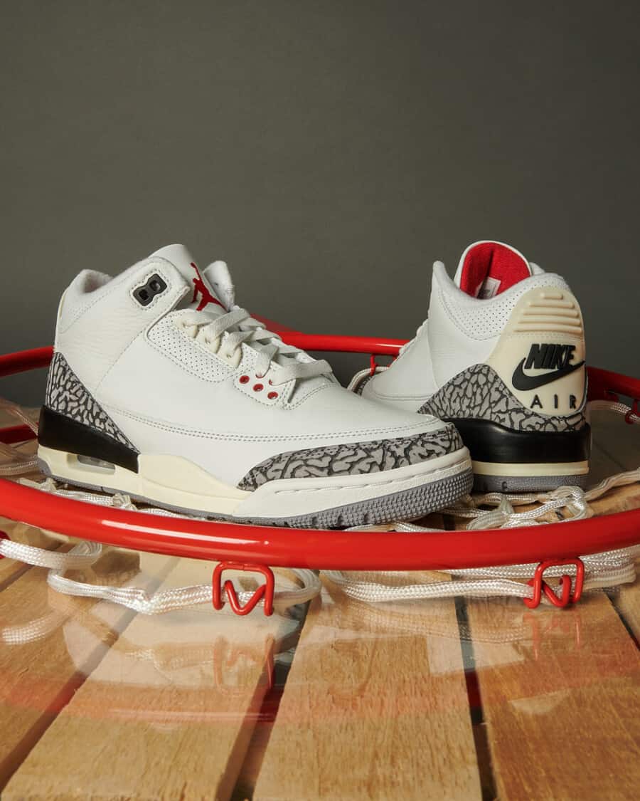 Air Jordan 3 Retro 'Reimagined White Cement' sneaker sitting in middle of basketball hoop on court