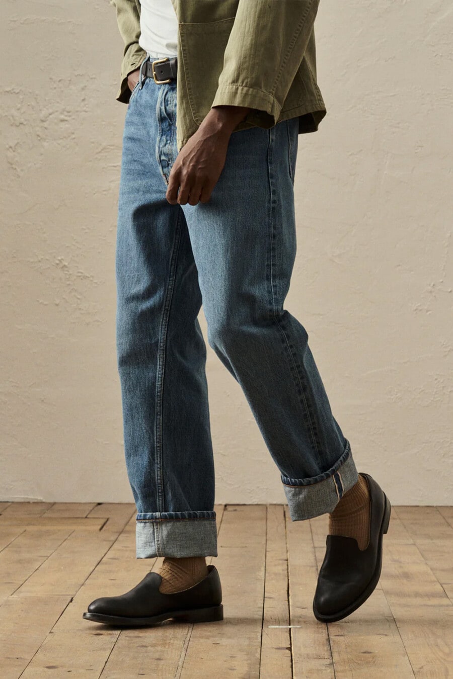 Close up of man wearing blue denim jeans with turn-ups with camel socks and black slip on loafers