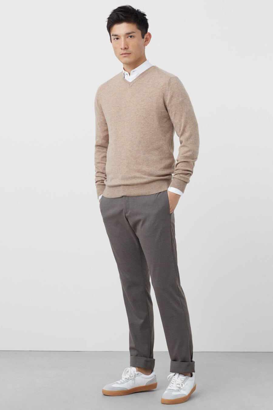 Men's grey chinos, white shirt, beige merino V-neck sweater and white sneakers outfit with no socks
