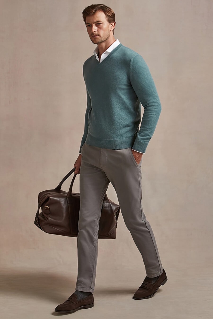Men's grey pants, white shirt, teal V-neck sweater, brown suede penny loafers and leather brown weekender bag