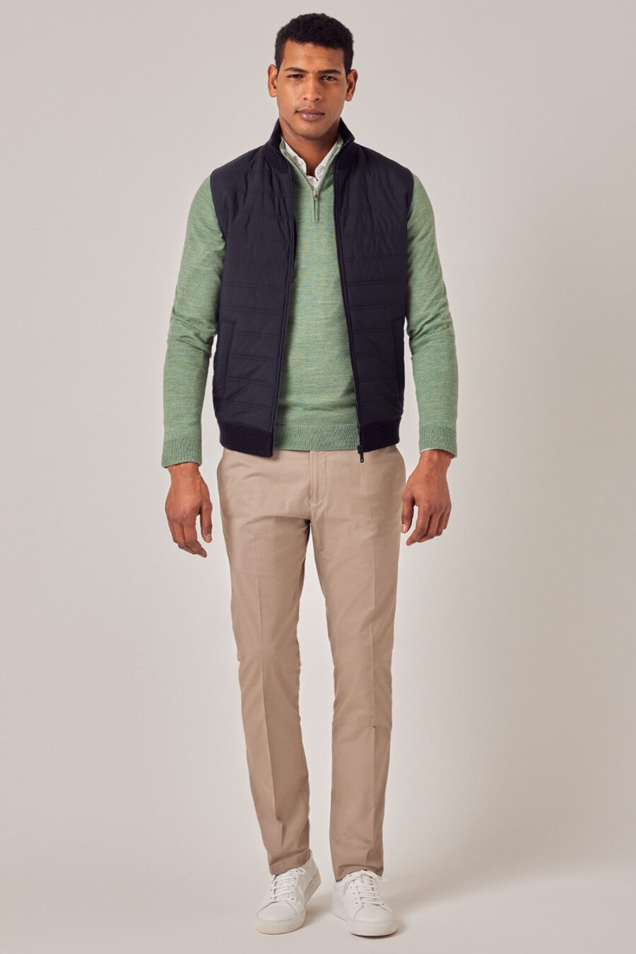 Men's khaki pants, white shirt, green quarter-zip sweater, navy vest and white sneakers outfit