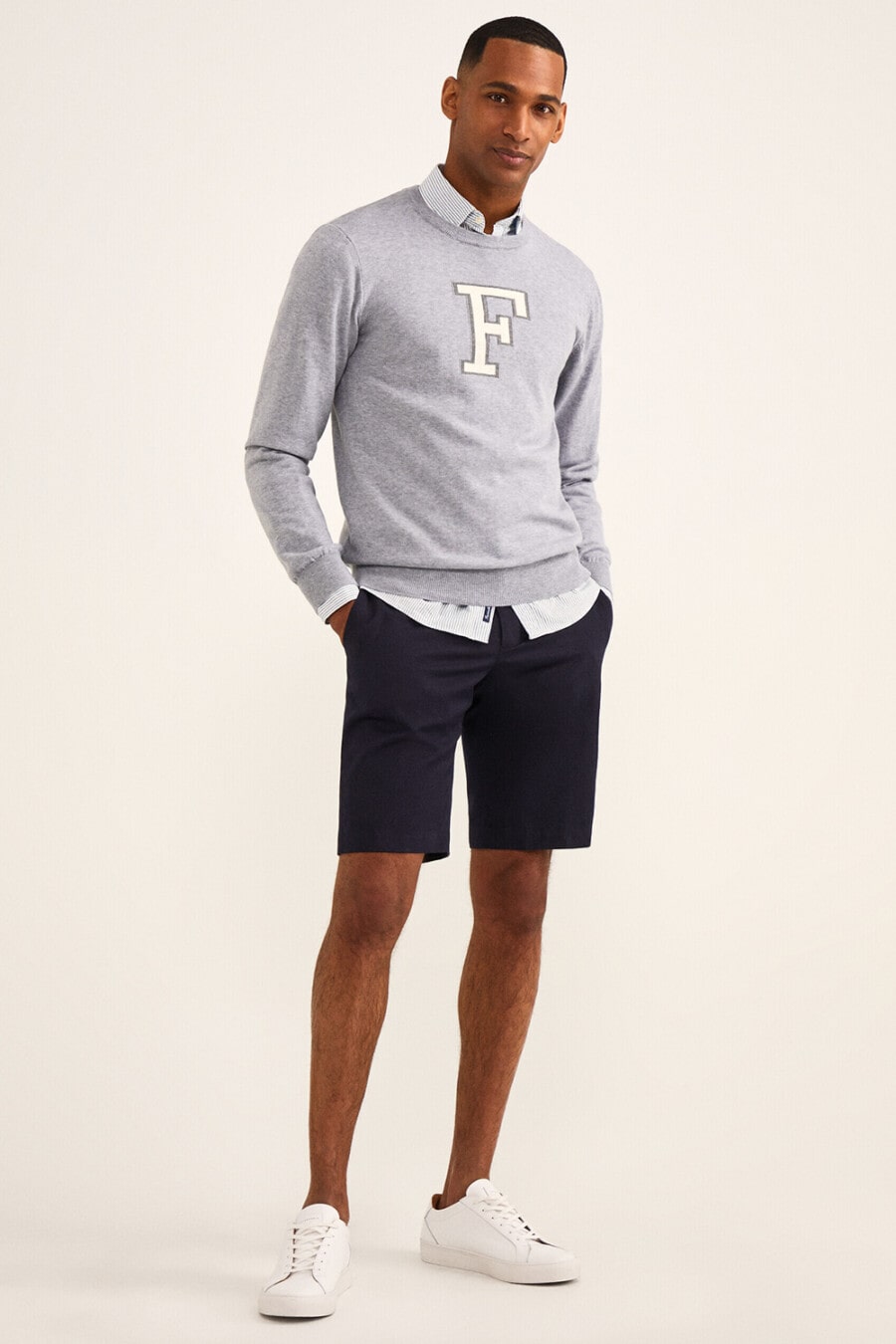 Men's navy chino shorts, sky blue shirt, grey collegiate sweater and white sneakers outfit