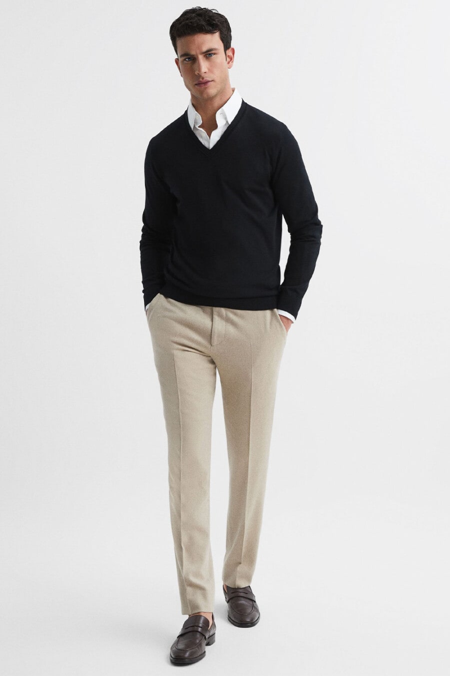 Men's beige tailored pants, white shirt, navy V-neck sweater and brown leather penny loafers outfit