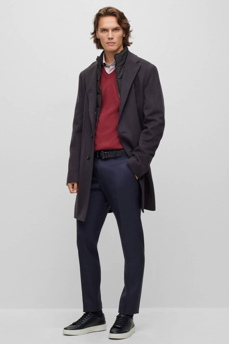 Men's navy tailored pants, pink shirt, burgundy V-neck sweater, navy trench coat and black leather sneakers outfit
