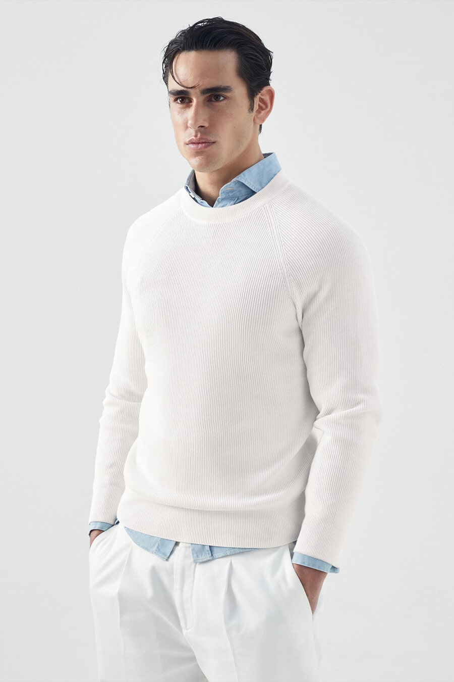 Man wearing blue denim shirt underneath a white ribbed sweater with white pants