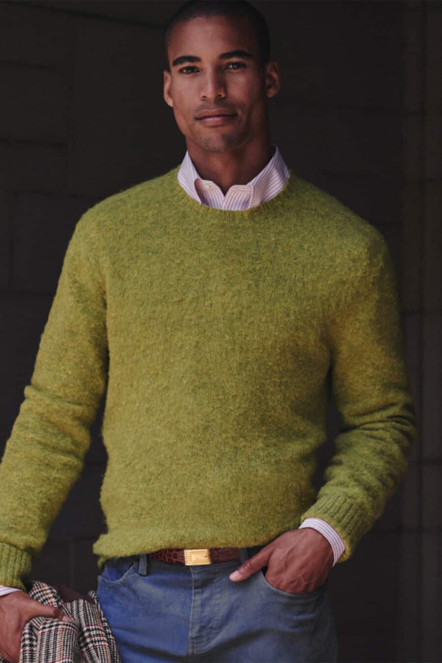 Man wearing blue jeans with a pink stripe shirt and green textured sweater