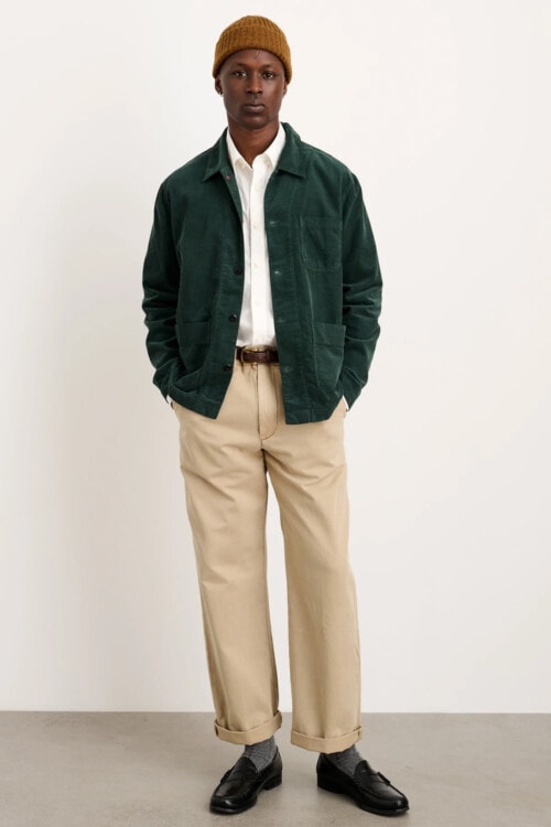 Men's khaki wide pants, white Oxford shirt, green chore coat, mustard beanie and black leather penny loafers outfit