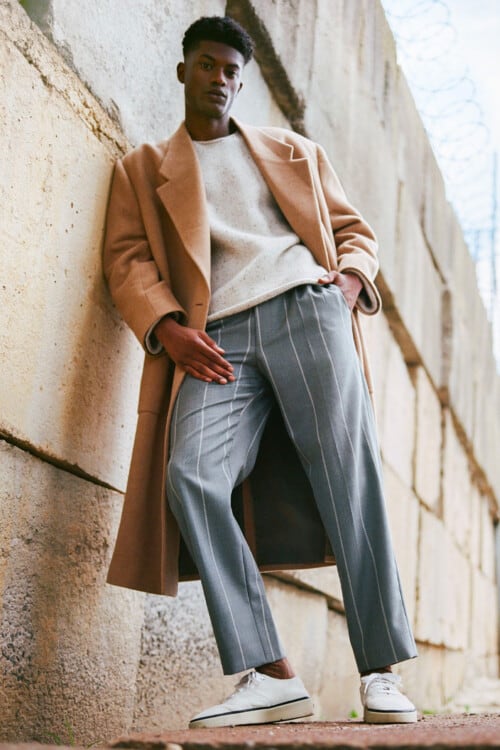 Men's grey pinstripe pants, beige sweater, camel overcoat and white skate sneakers outfit