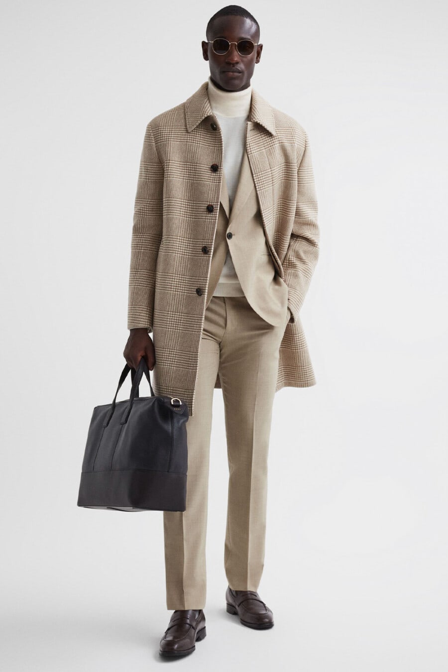 Men's cream/beige suit, off-white turtleneck, beige check overcoat, brown leather penny loafers and brown leather weekender bag outfit