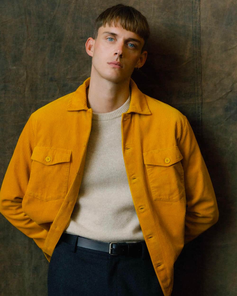 Man wearing a mustard corduroy shacket over a beige crew neck sweater tucked into navy pants