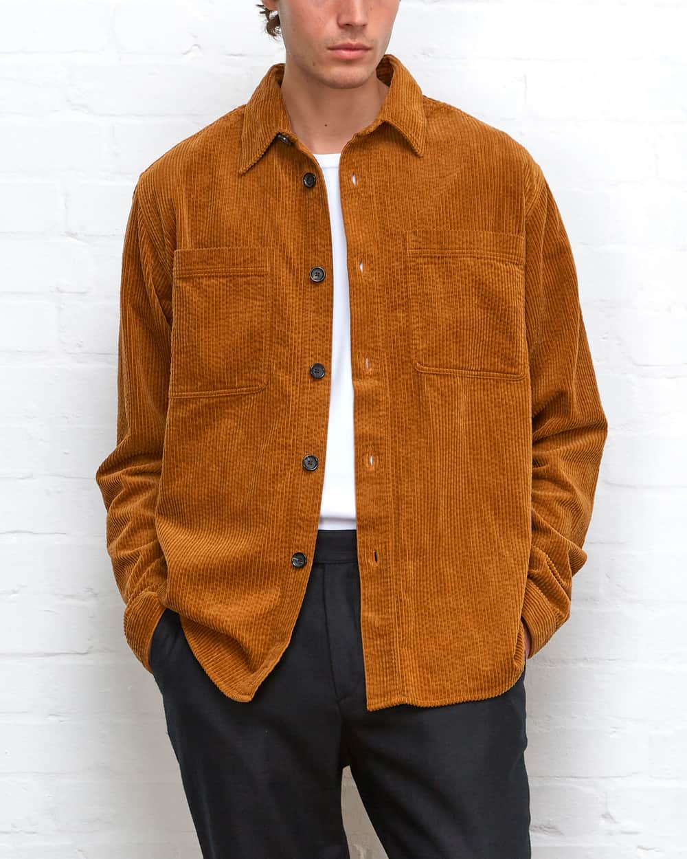 Man wearing a brown/burnt orange corduroy overshirt over a white T-shirt tucked into black tailored pants