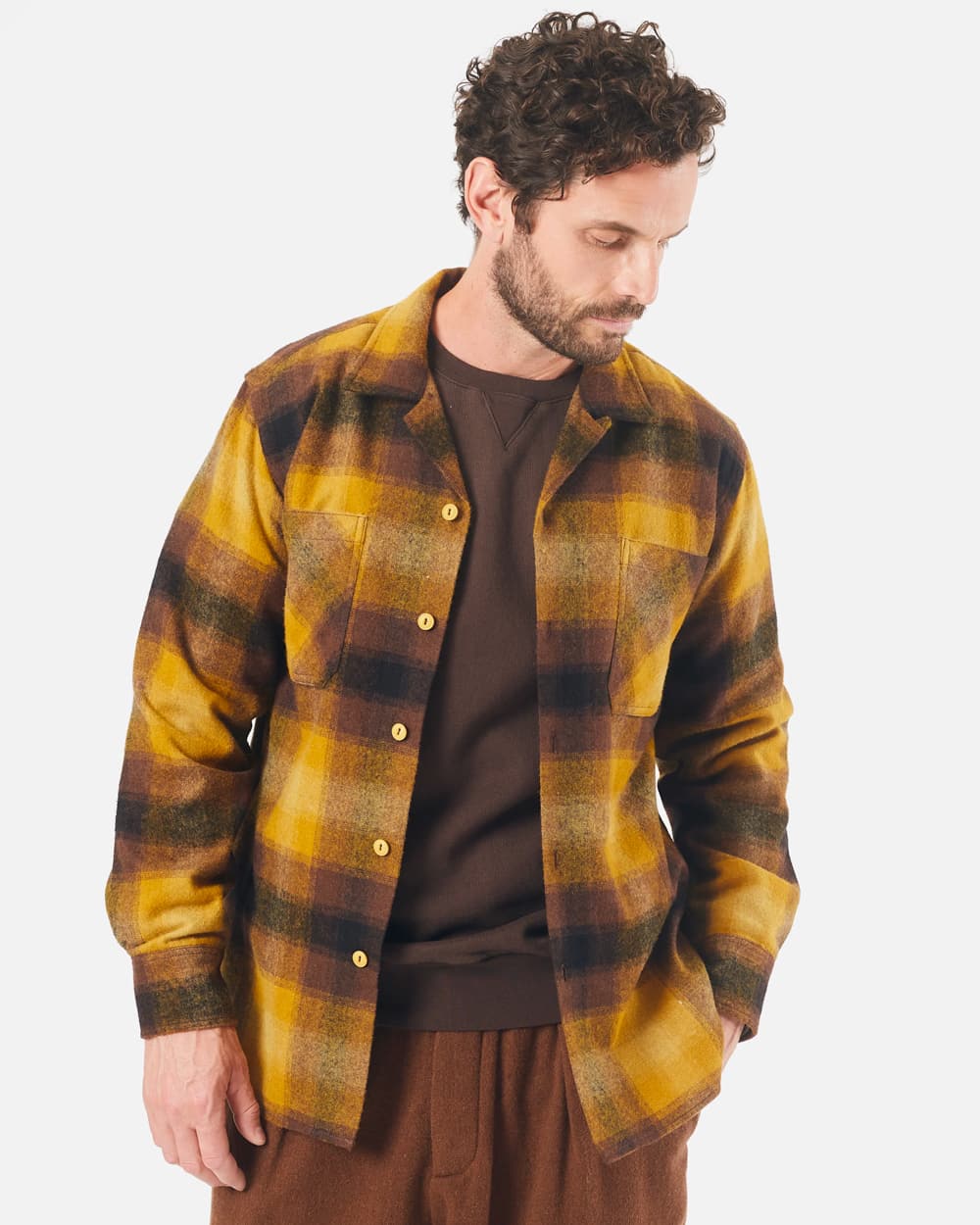 Man wearing a Universal Works mustard/brown checked shacket over a brown sweatshirt with brown wide-fit pants