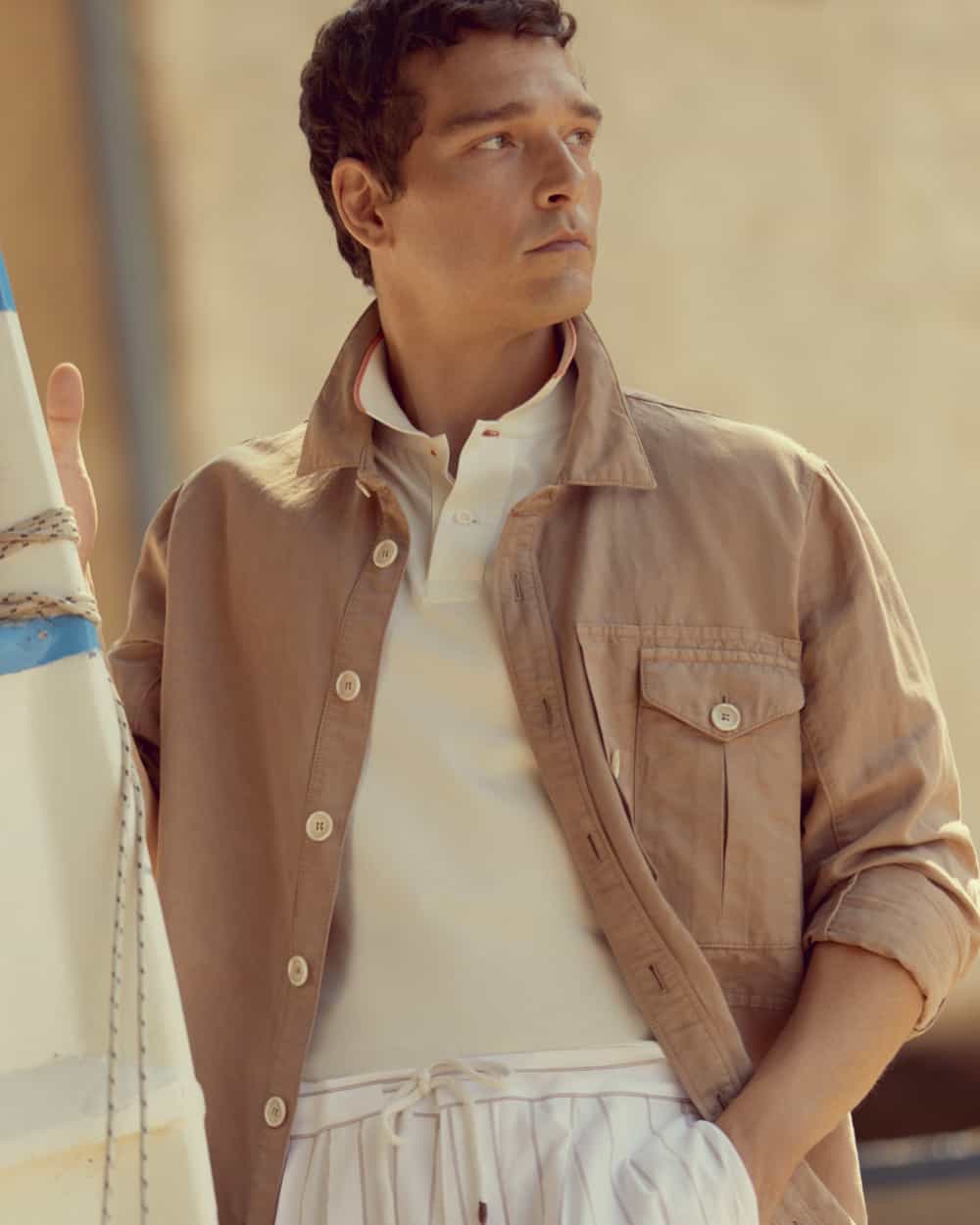 Man wearing white striped drawstring pants, knitted off-white polo shirt and light brown shacket by Brunello Cucinelli