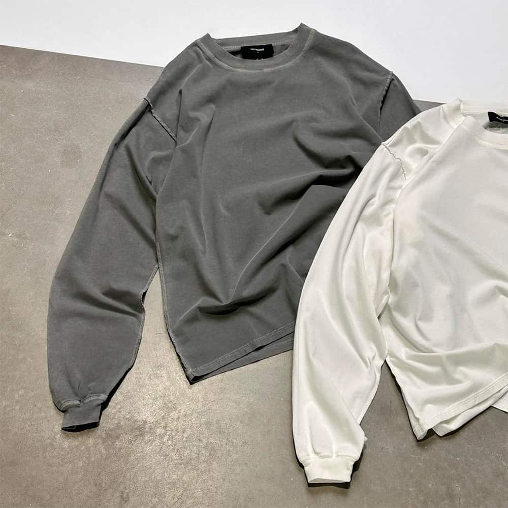 Two oversized Represent sweatshirts in dark grey and white laid out on concrete floor