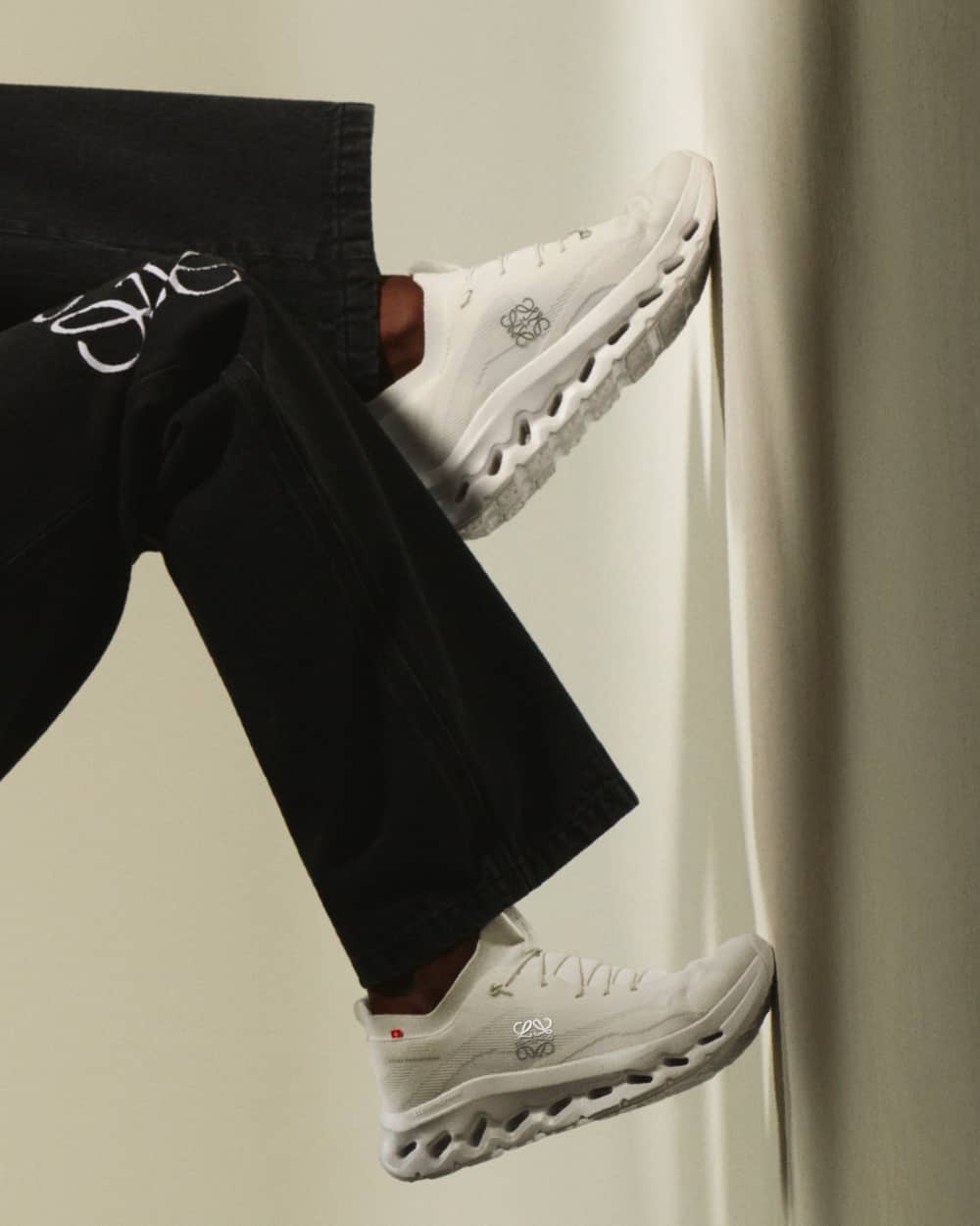 Man wearing Loewe x On Cloudtilt sneakers on feet with no socks and black pants