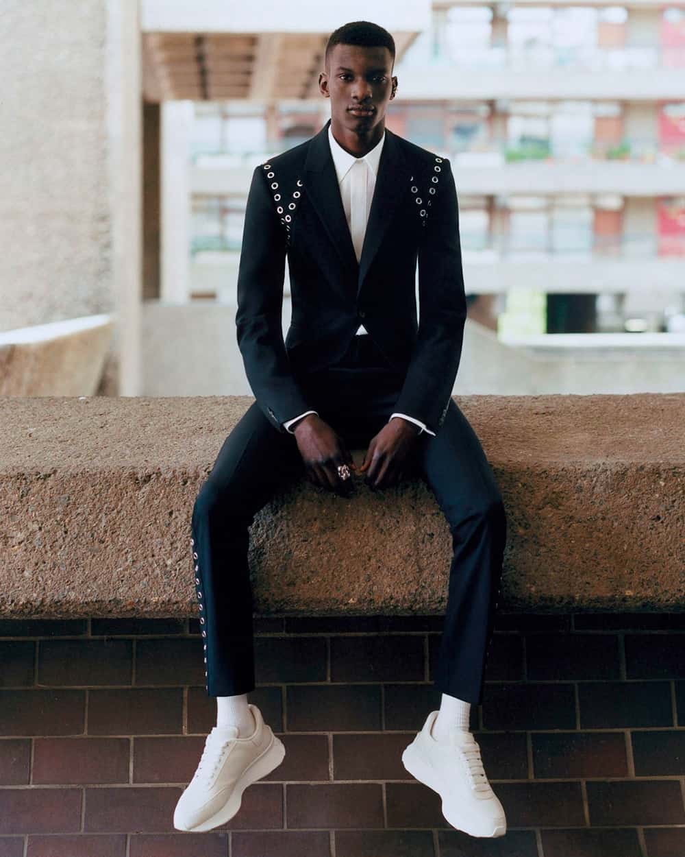 Black man wearing Alexander McQueen black suit with white shirt and white sneakers