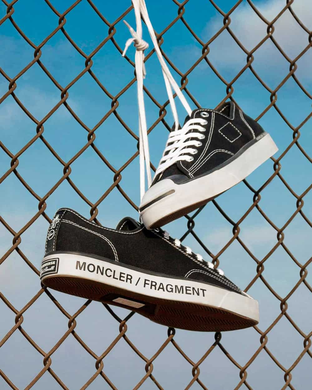 A pair of Moncler x Fragment black low-top canvas sneakers hanging on wire fence by laces