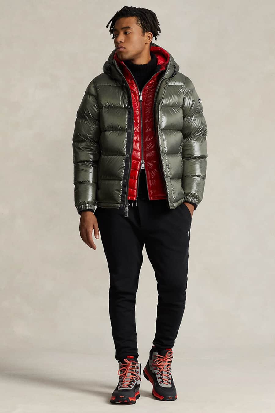 Men's black sweatpants, black top, red puffer vest, green puffer jacket and technical hiking boots outfit