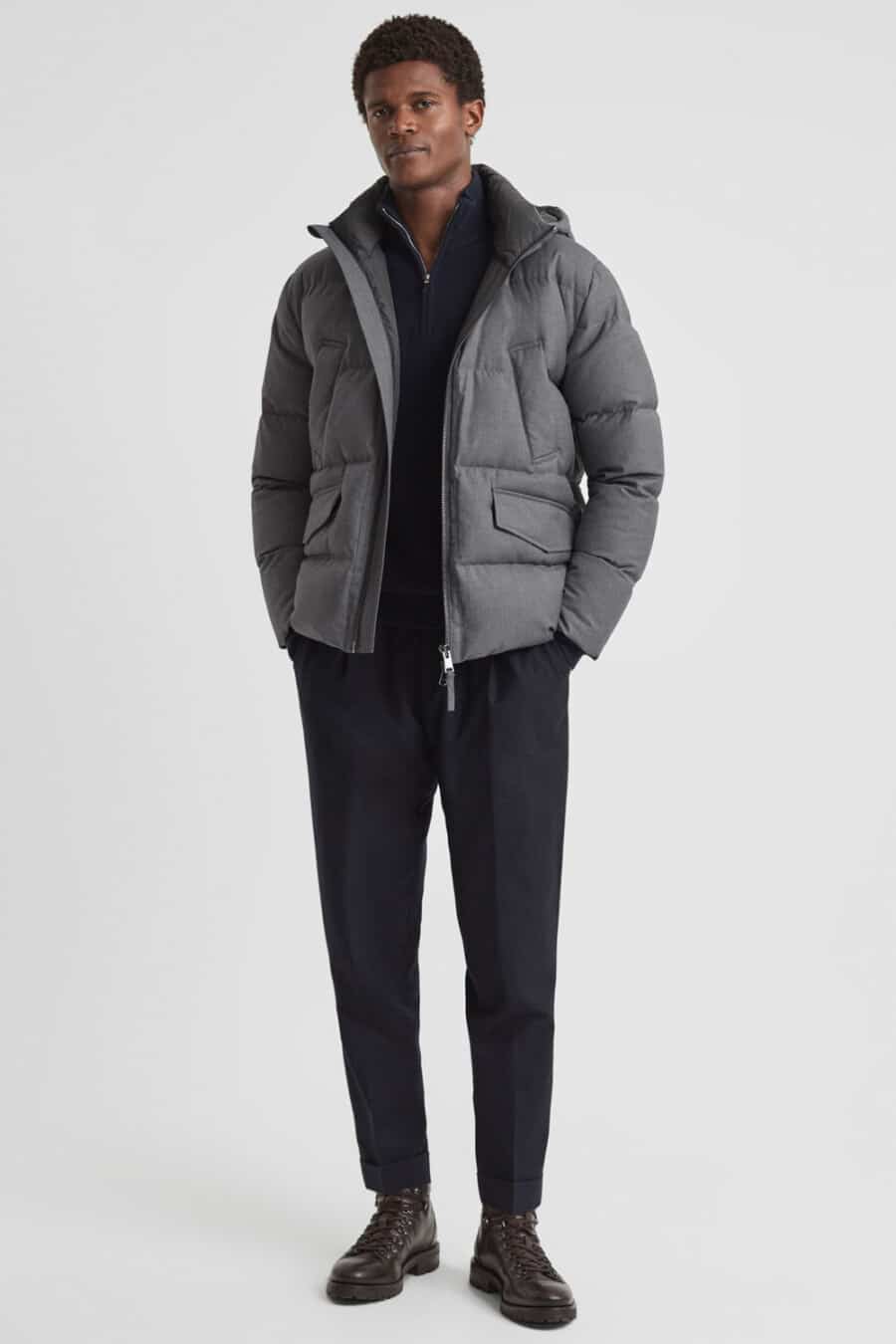 Men's navy tailored pants, navy zip neck sweater, grey puffer jacket and brown leather boots outfit