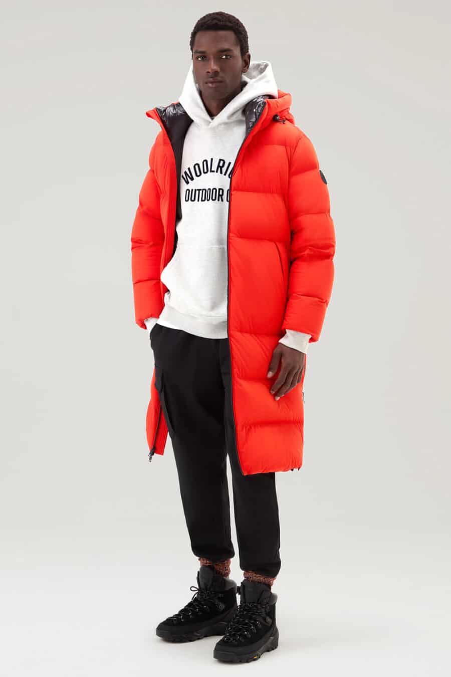 Men's black cargo pants, white logo hoodie, long length bright red puffer jacket, orange marl hiking socks and black hiking boots outfit