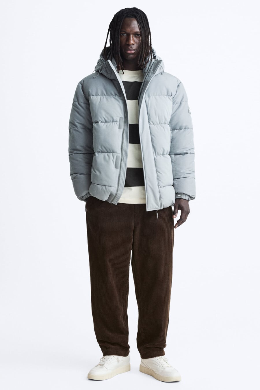 Men's wide-fit brwon pants, white/black striped top, light blue puffer jacket and chunky white sneakers outfit