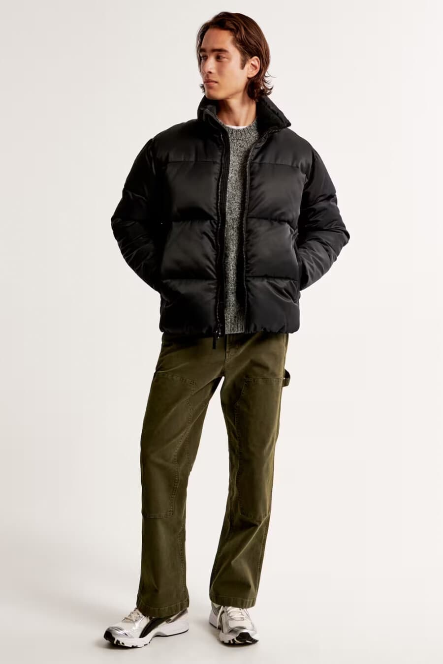 Men's green carpenter pants, white T-shirt, grey textured sweater, black puffer jacket and white/black sneakers outfit