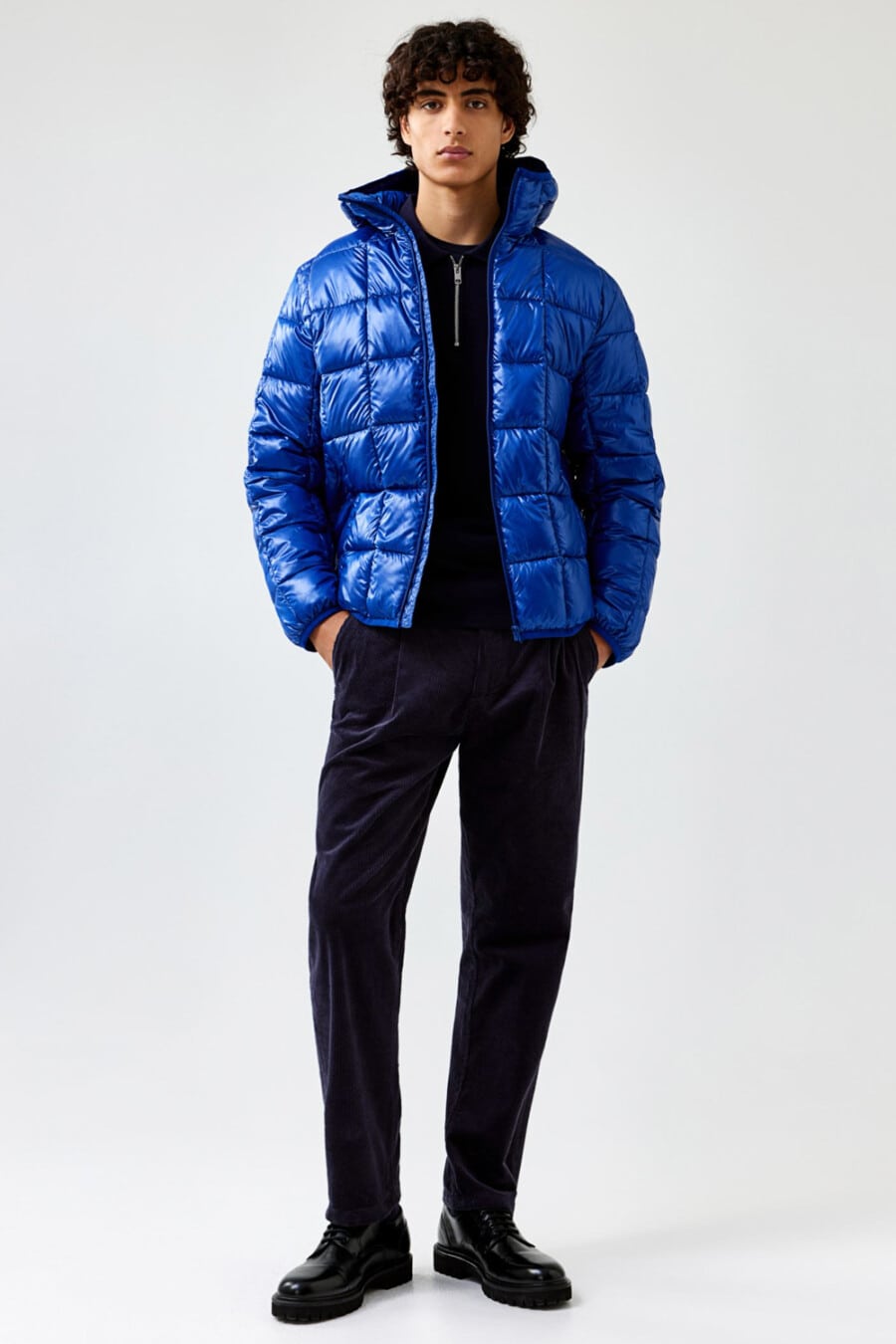 Men's navy corduroy trousers, navy zip-neck sweater, bright blue puffer jacket and black chunky shoes outfit