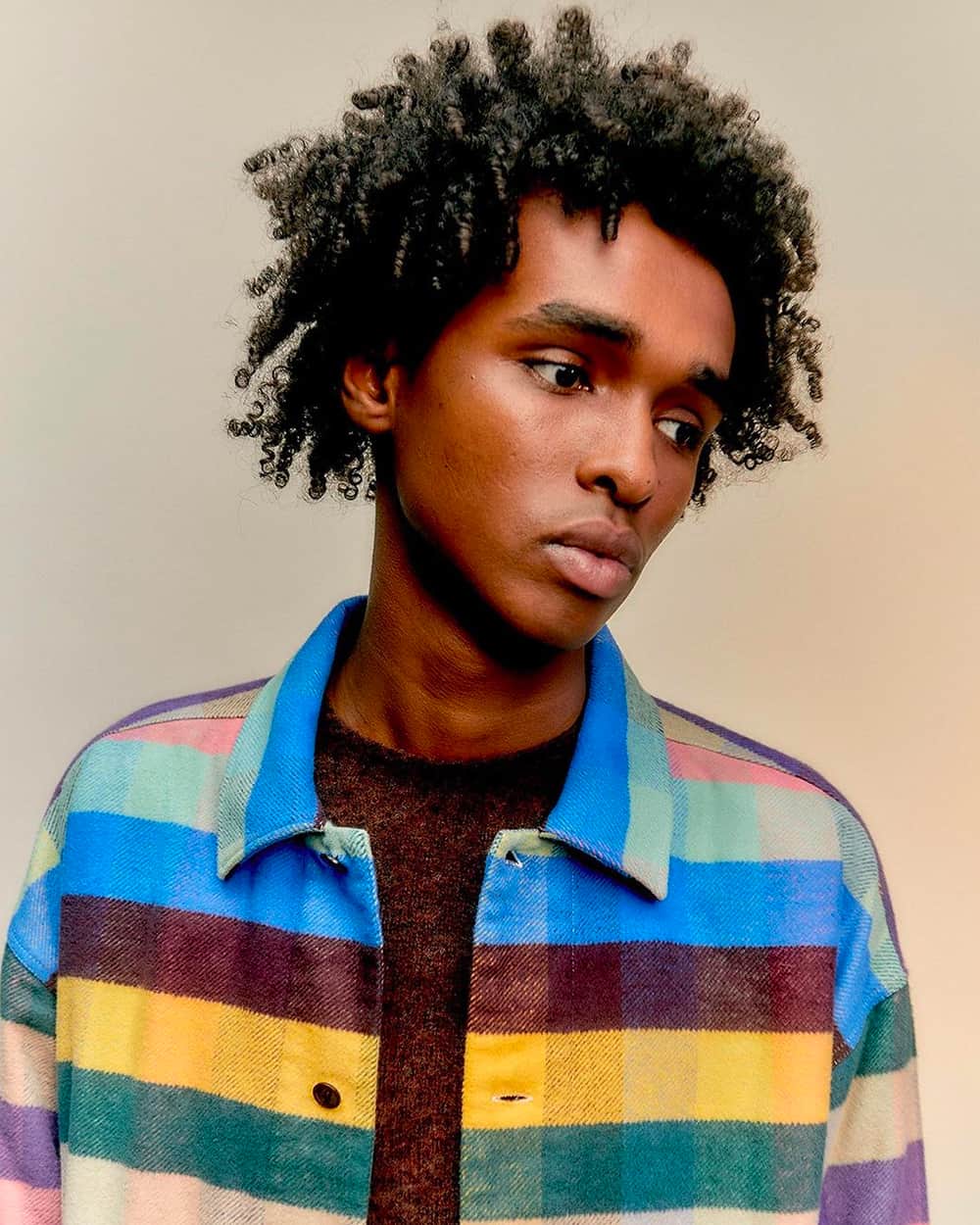 Black man wearing a bright multicolored flannel shirt by YMC over a burgundy T-shirt