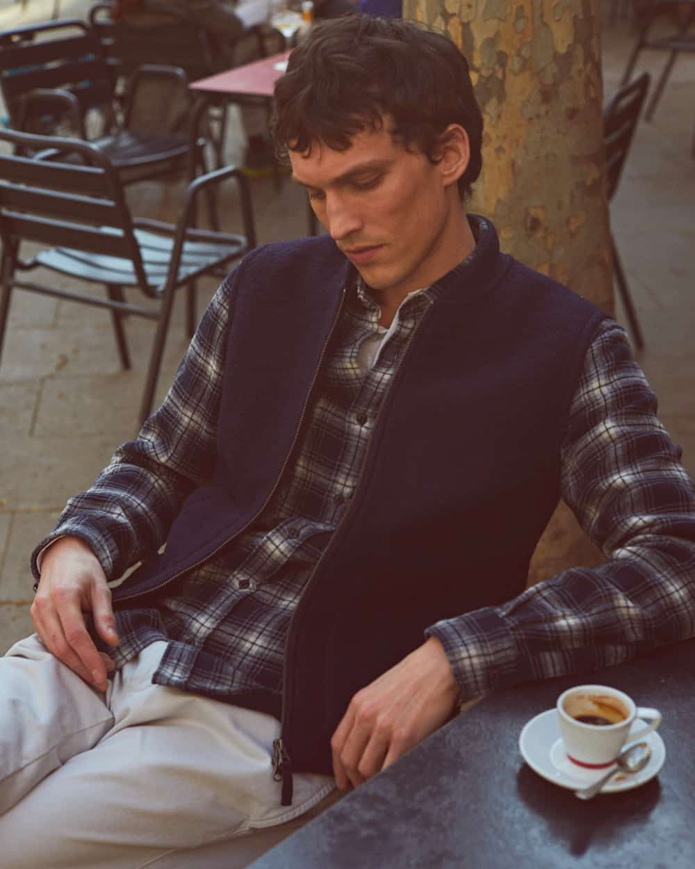 Man sitting having coffee wearing a Hartford blue/white check flannel shirt under a navy vest with light grey pants