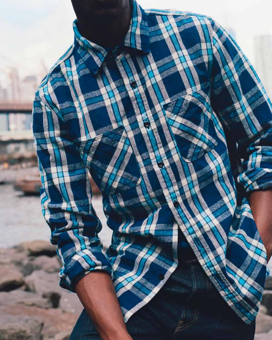 Close up of a black man wearing an Alex Mill blue check flannel shirt with raw denim jeans