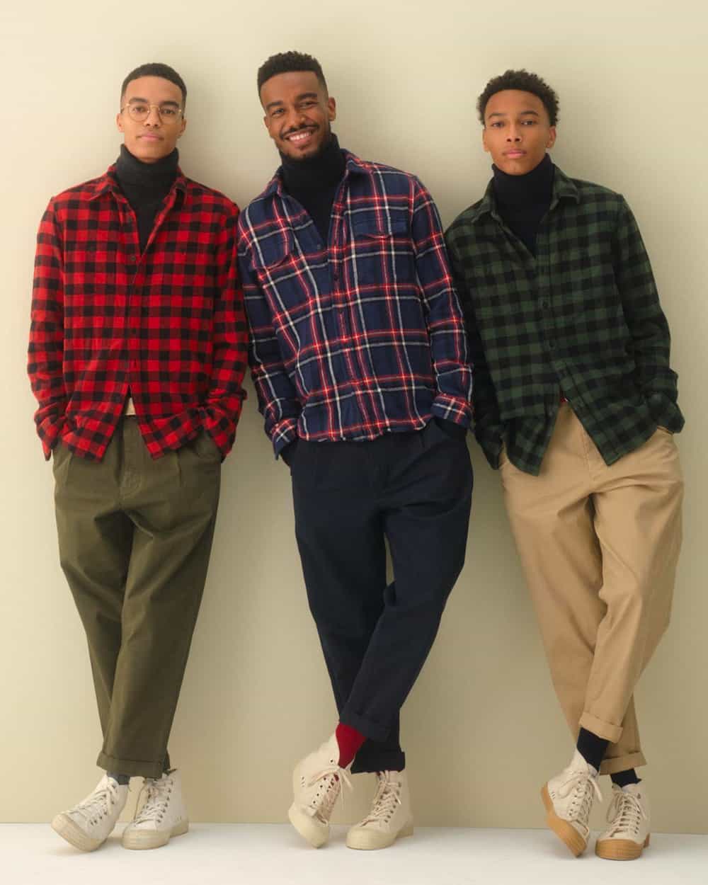 Three black men wearing Alex Mill check flannel shirts over black turtlenecks with varying colored pants