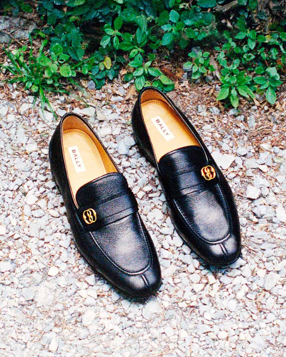A pair of luxury men's Bally black leather loafers with gold logo on stones outside