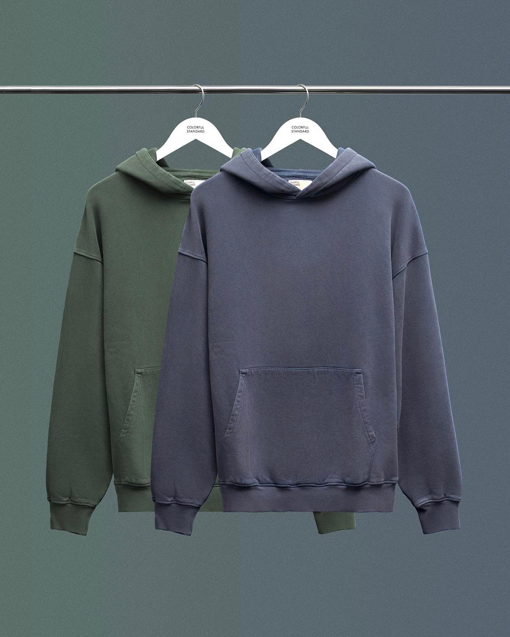 Two Colorful Standard oversized hoodies in green and blue hanging on a rail