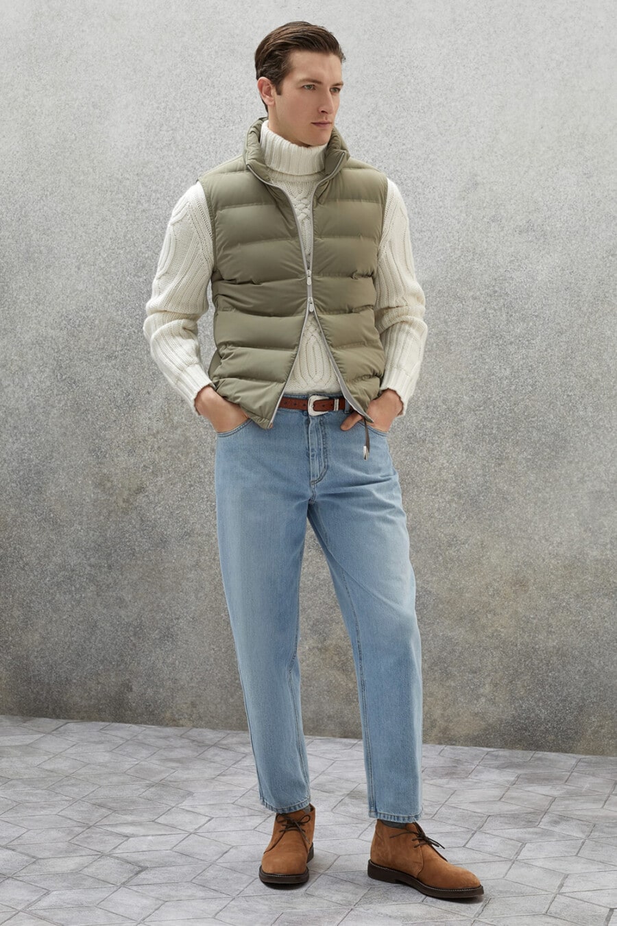 Men's light wash jeans, white chunky turtleneck, green puffer best and brown suede chukka boots outfit