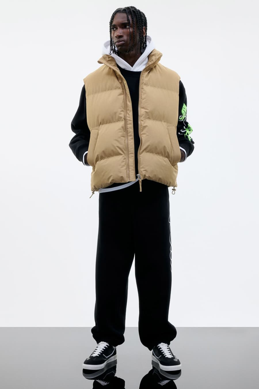 Men's baggy black pants, white hoodie, black long-sleeve top, oversized camel puffer vest and black sneakers outfit